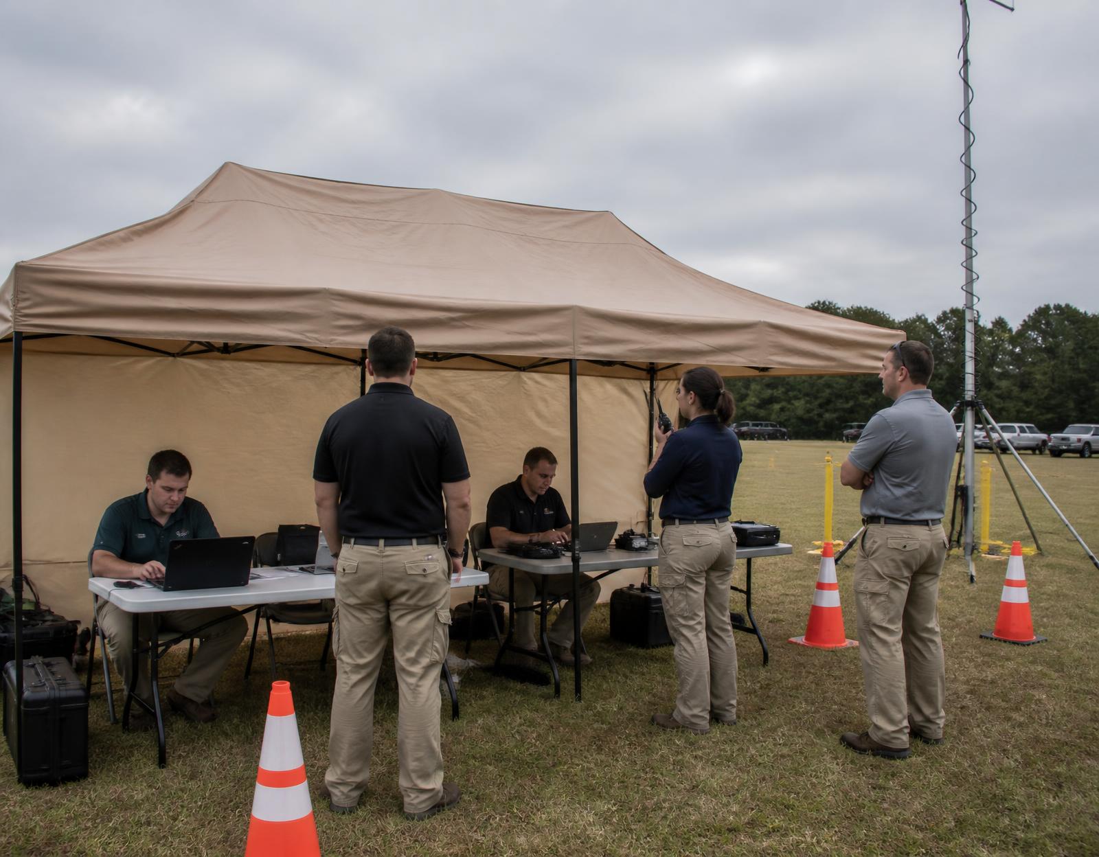 Mobile command tent at a field exercise with folding tables, laptops, radios and a portable mast antenna