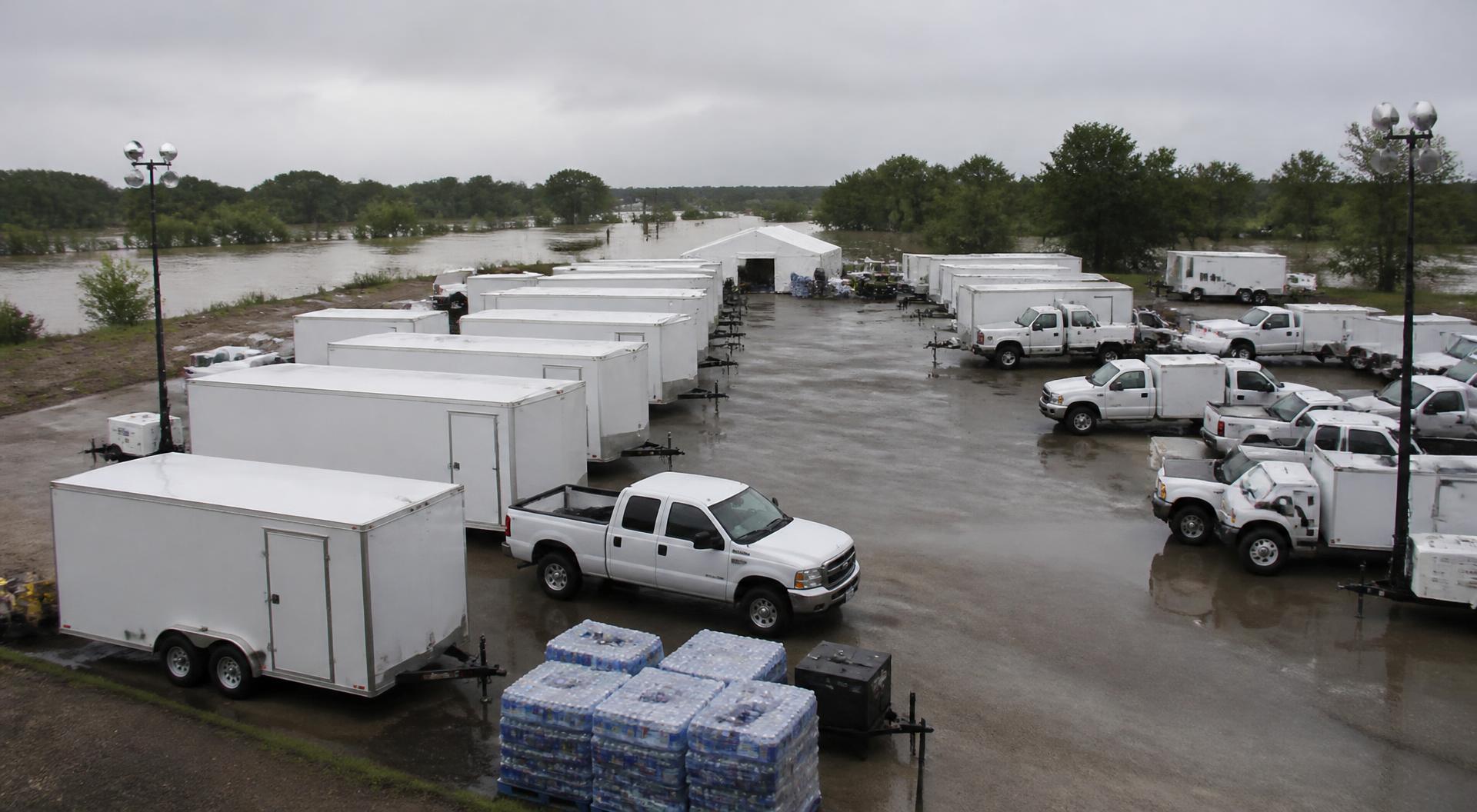 State emergency response staging area after a hurricane with rows of white trailers, light towers and shrink-wrapped supply pallets under an overcast sky